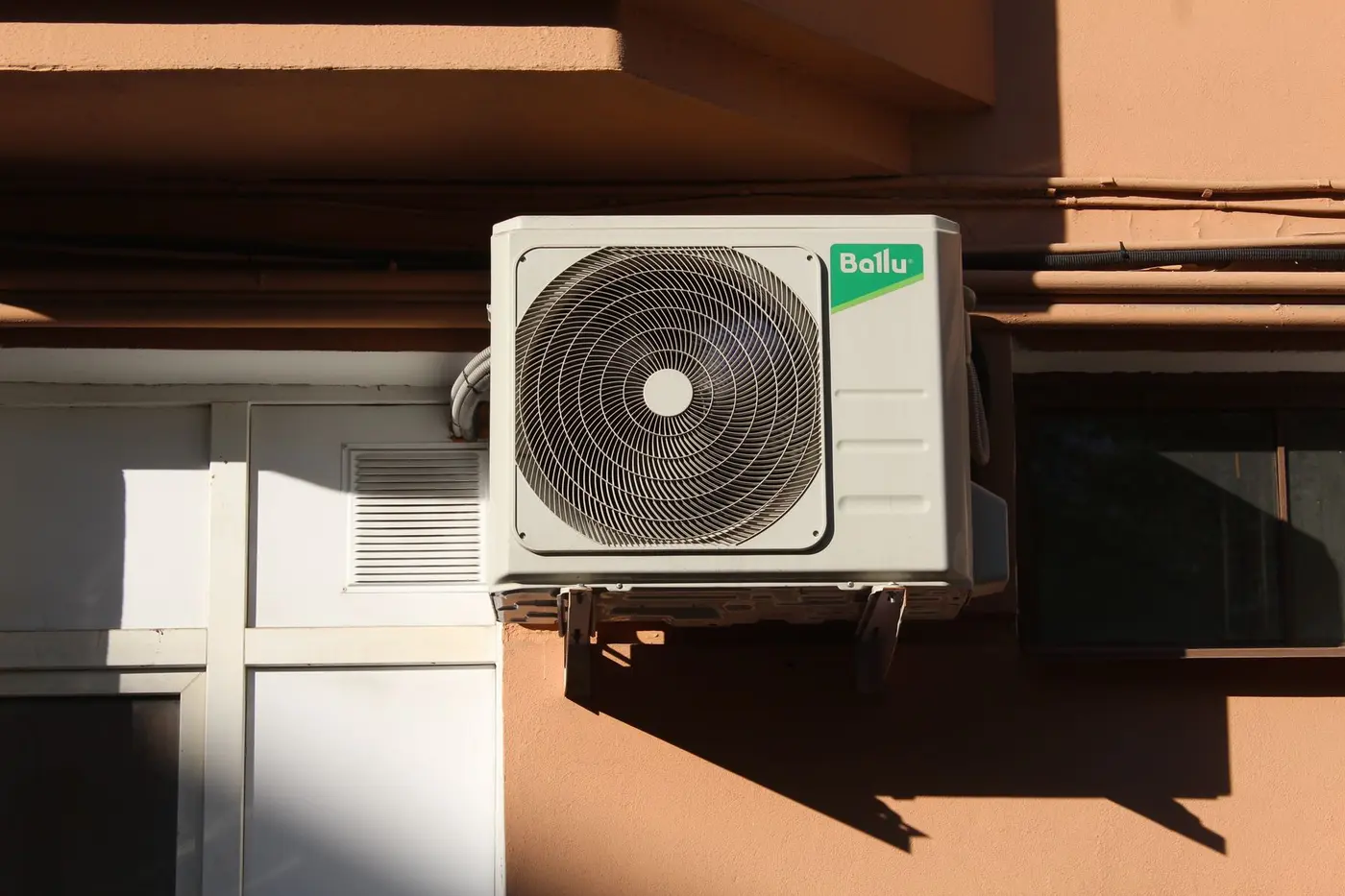 Air conditioner condenser unit mounted on an exterior wall in afternoon light