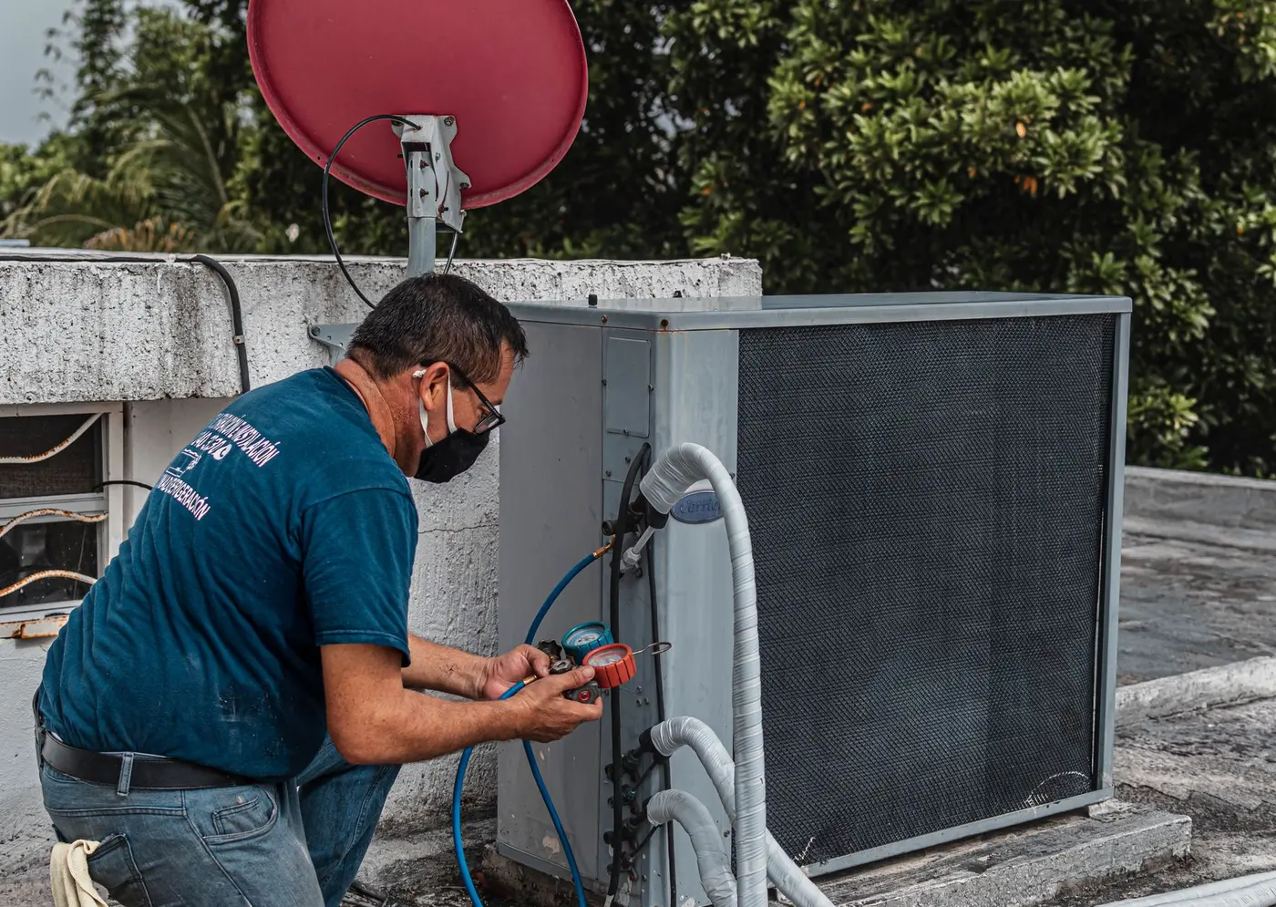 Technician checking refrigerant pressure on an outdoor air conditioner with a manifold gauge