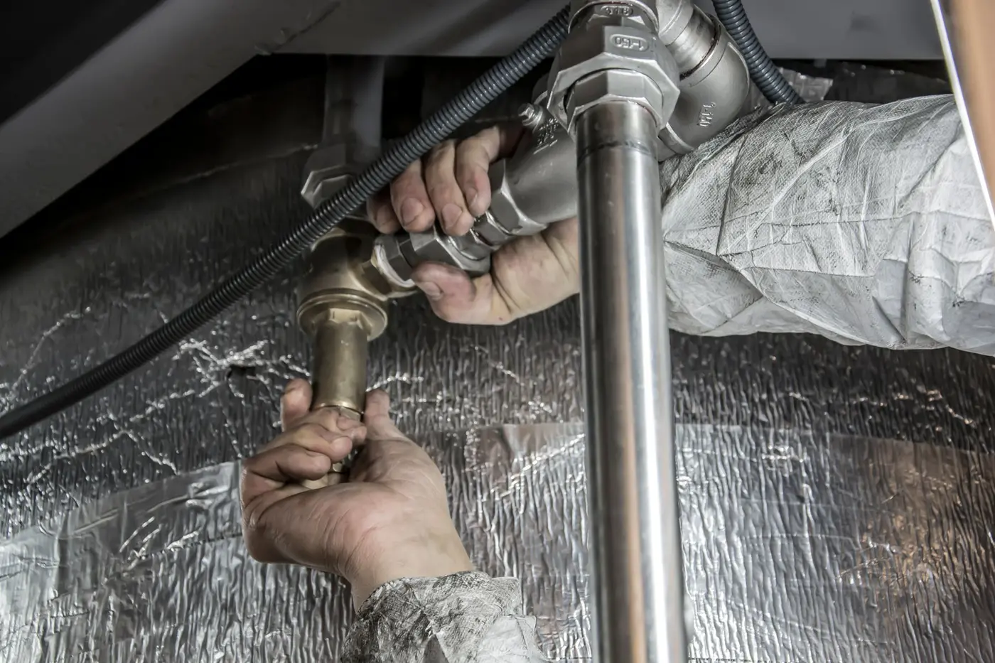 Plumber's hands tightening a brass fitting on pipework under a unit