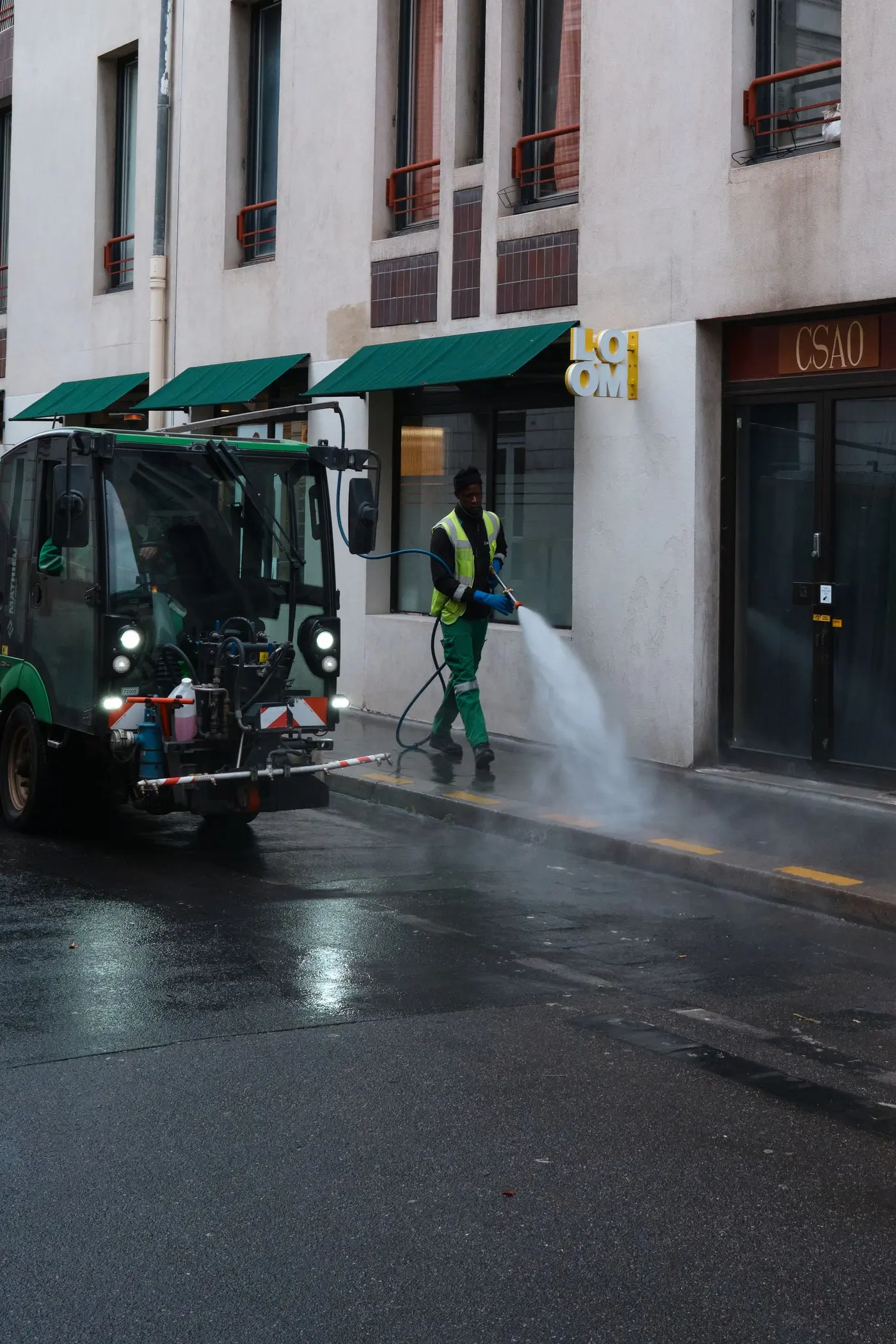 Worker running high-pressure water spray equipment across a hard surface