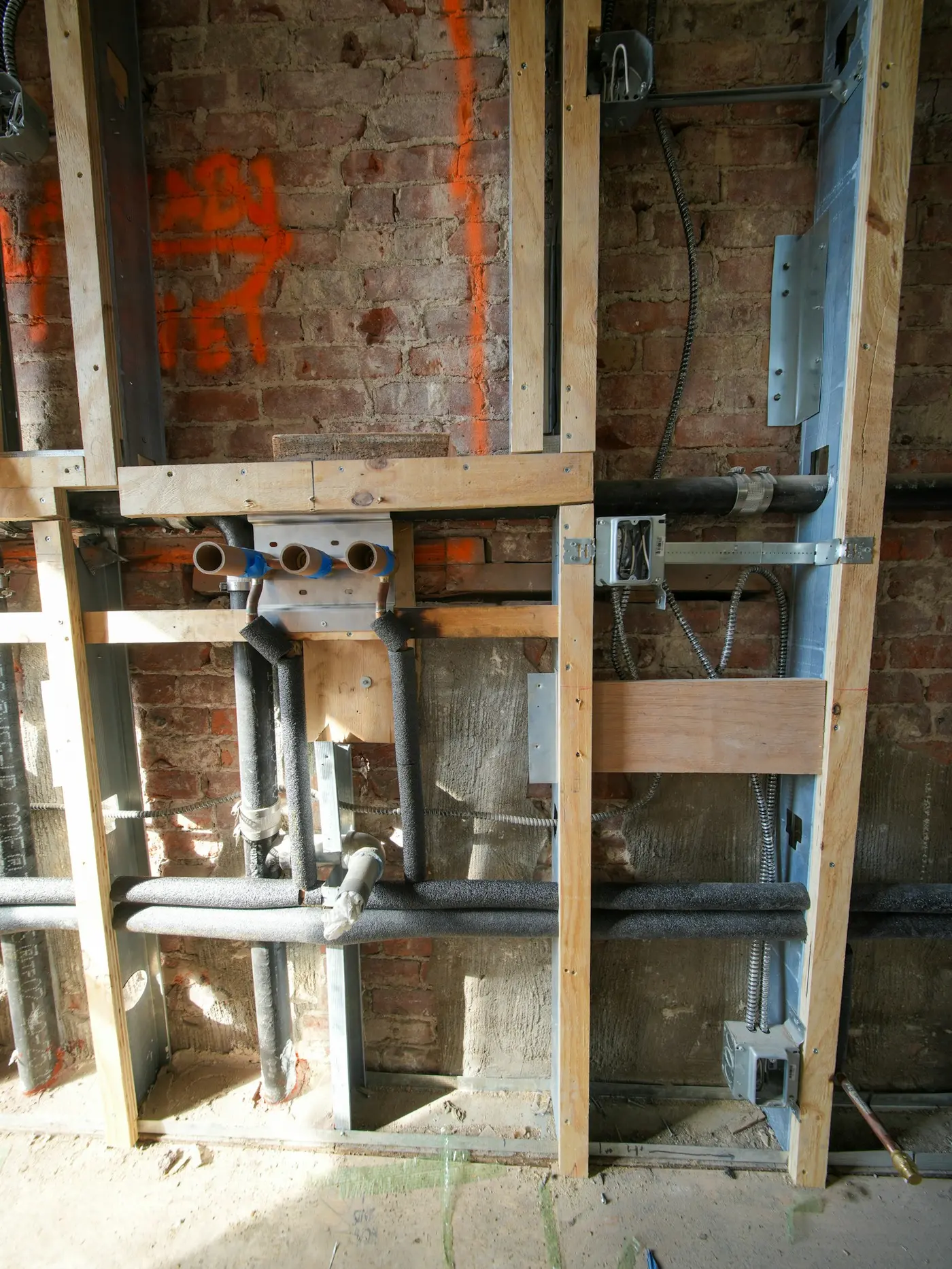 Copper pipe runs and conduit routed through wood wall framing mid-renovation