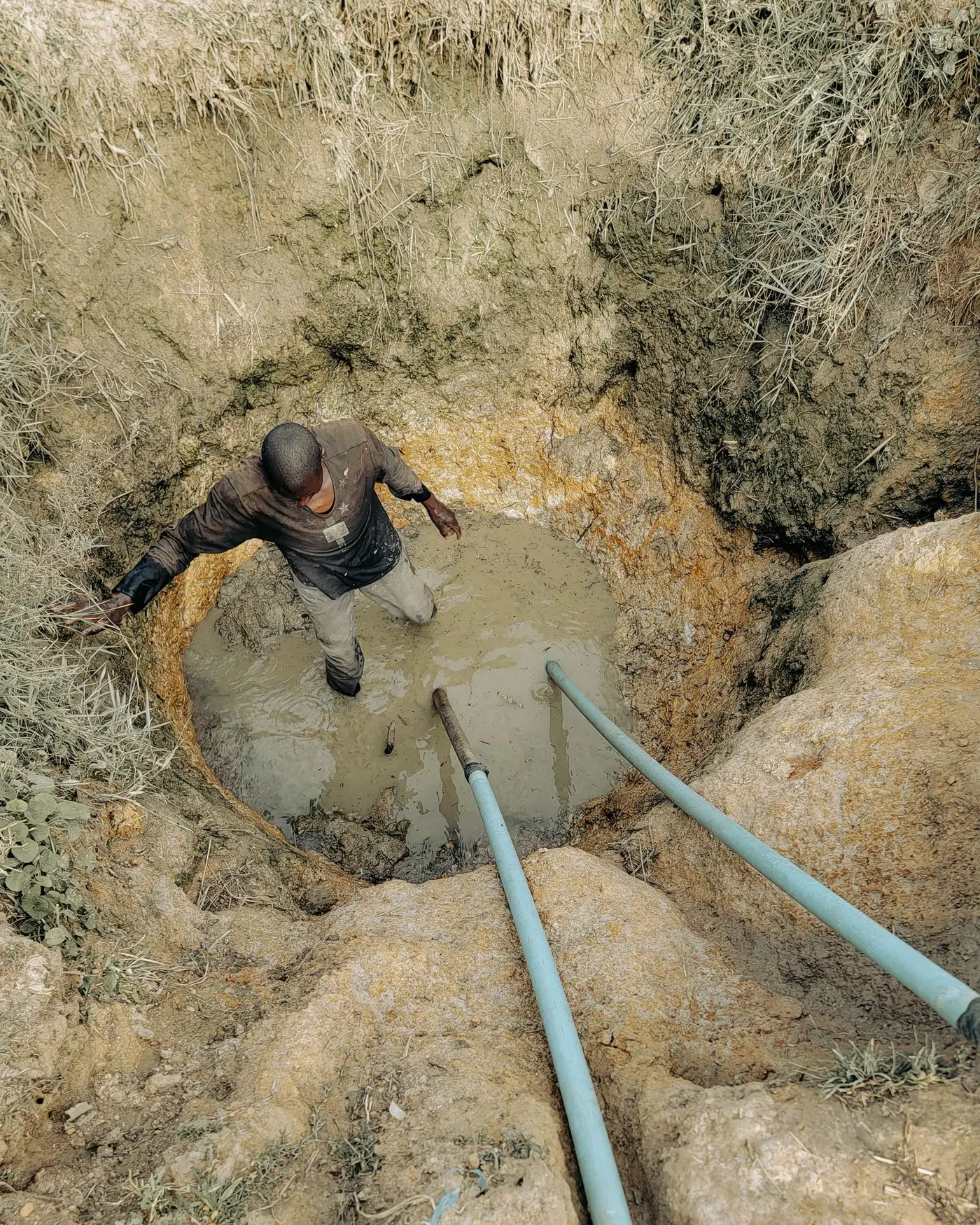 Worker standing in a muddy excavation pit with water service pipe laid in